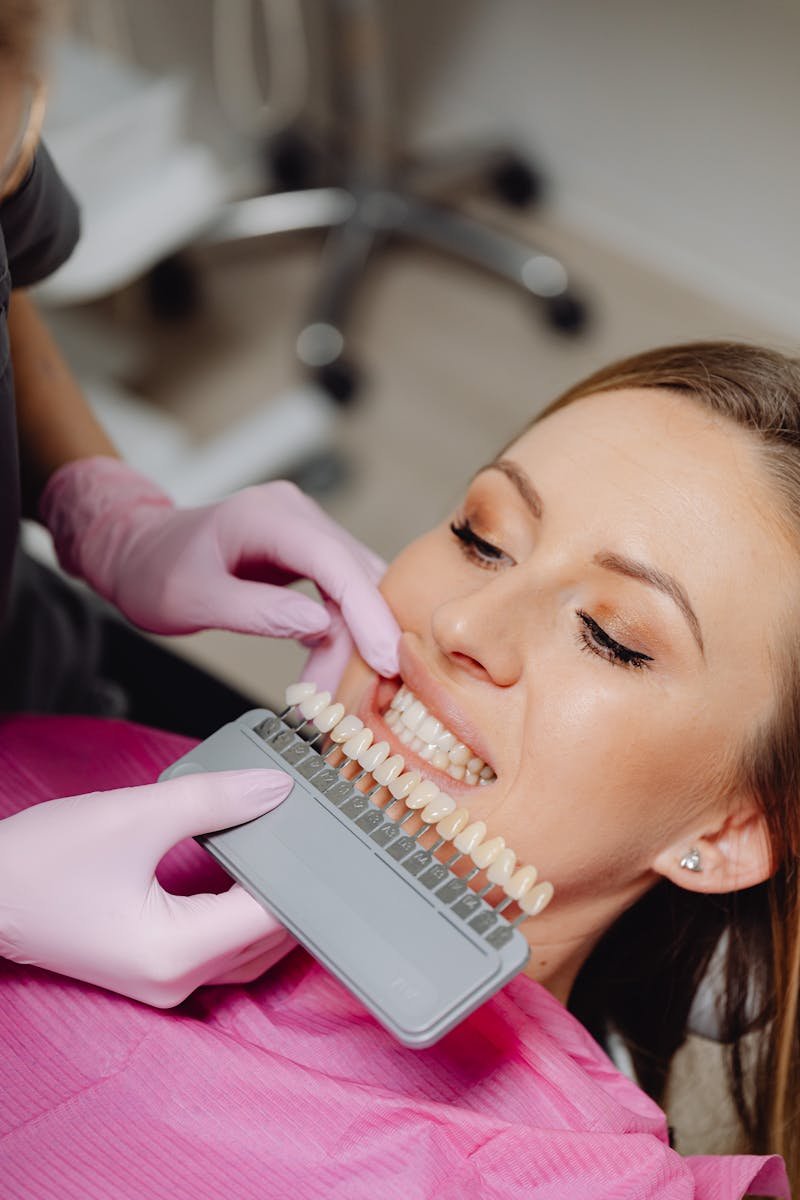 A woman undergoing a dental check-up with a shade guide to match teeth color in a dental clinic.